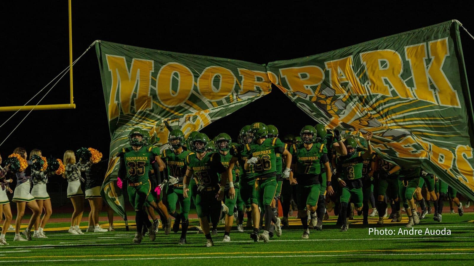 Moorpark football team running onto the field through the Moorpark banner