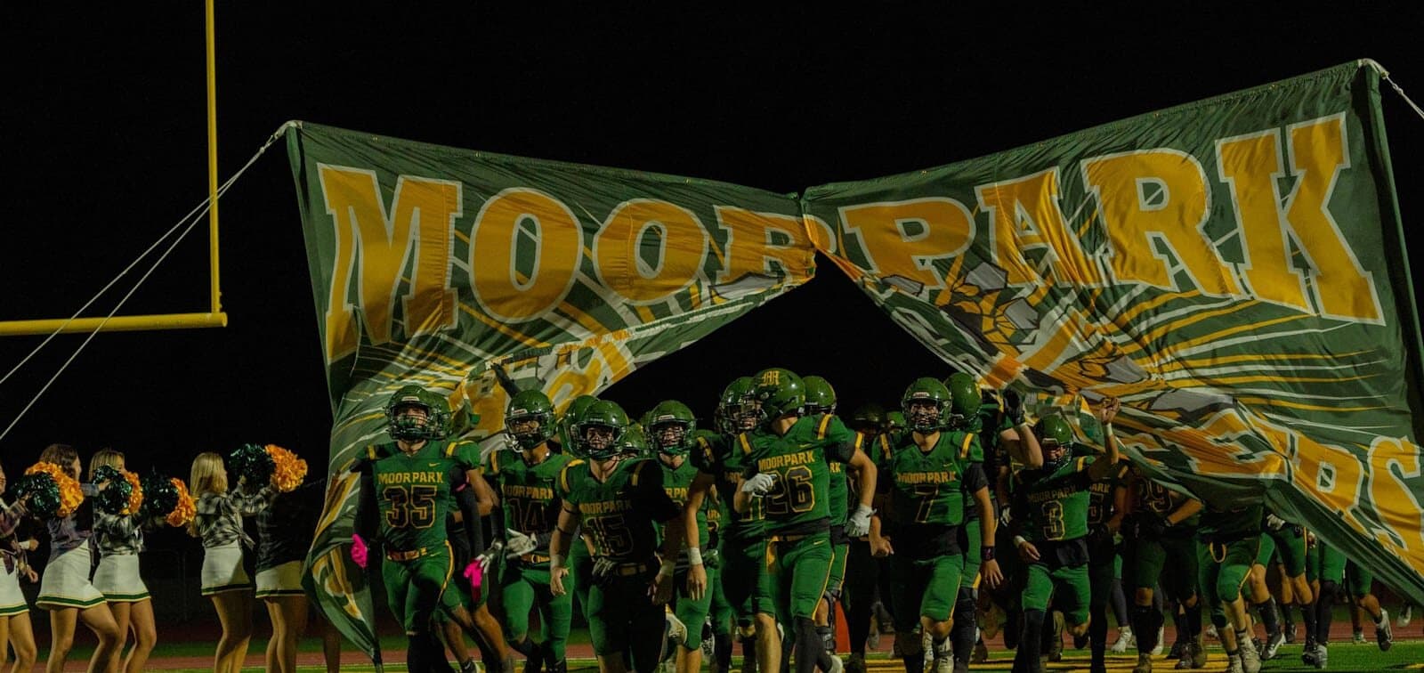 The Moorpark Musketeers football team running onto the field through the Moorpark banner